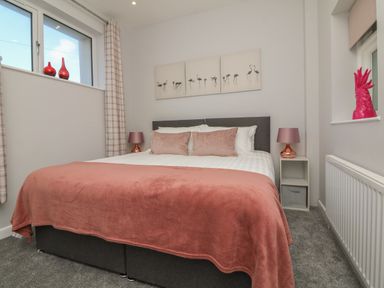 A bedroom with a double bed two bedside tables and lamps with pink accents at The Old Coach House in Braunton