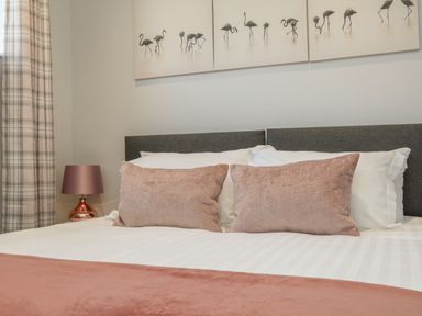A bedroom with a bed featuring pink pillows and a pink blanket with a flamingo wall art above at The Old Coach House in Braunton