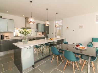 A kitchen with a dining table and chairs a kitchen island with a flower vase and hanging lights at The Old Coach House in Braunton