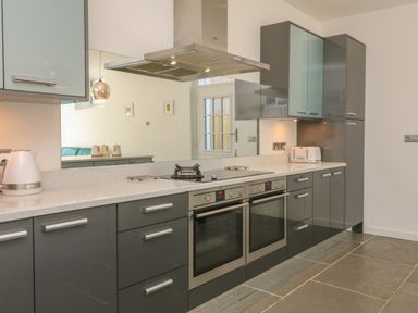 A kitchen with grey cabinets two built in ovens and a stovetop at The Old Coach House in Braunton