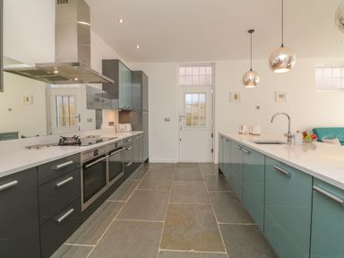A kitchen with a stove oven and cabinets on the left and a sink with pendant lights on the right at The Old Coach House in Braunton