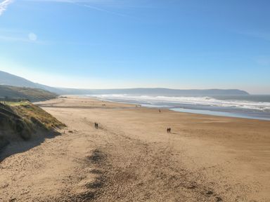 A wide sandy beach with people walking near the water and dunes on the left side at The Old Coach House in Braunton