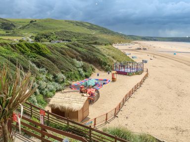 A beach with a fenced children play area and hills in the background at The Old Coach House in Braunton