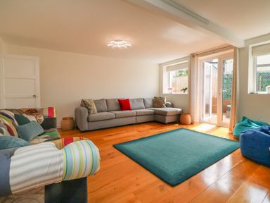 A living room with a grey sectional sofa a multicolor patchwork sofa a blue rug wooden floor and glass doors at The Old Coach House in Braunton