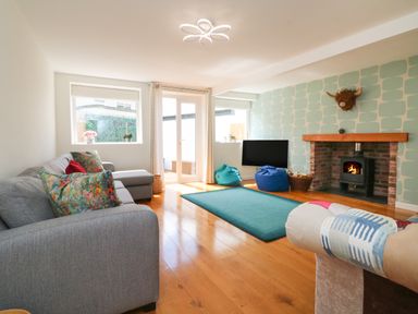 A living room with a gray sectional sofa colorful pillows a fireplace a mounted television bean bags and wooden flooring at The Old Coach House in Braunton