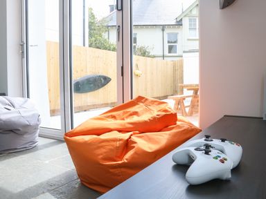 A room with two bean bags and two white game controllers on a table near glass doors that lead to a fenced patio with a picnic table at The Old Coach House in Braunton