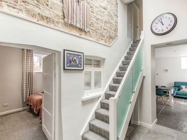A staircase with glass panel railing next to a hallway and a bedroom entrance at The Old Coach House in Braunton