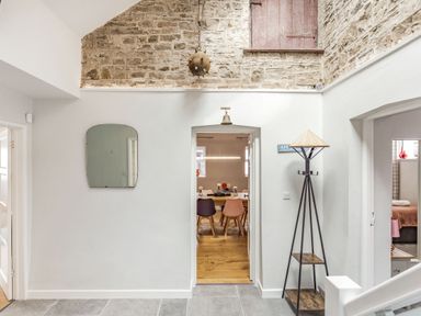 A hallway with a mirror on the wall a hanging light a coat rack and visible rooms beyond at The Old Coach House in Braunton