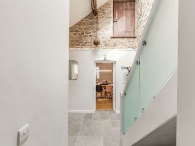 A hallway with gray tile floor a staircase with frosted glass panels and a view through a doorway to a dining area at The Old Coach House in Braunton