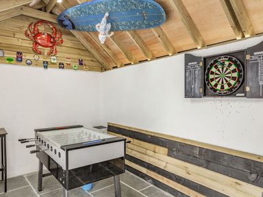 A dartboard and foosball table in a wooden game room with decorative crab and surfboard at The Old Coach House in Braunton