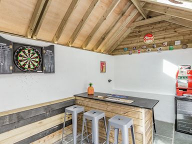A small bar area with a dartboard stools and vintage signs on wooden walls at The Old Coach House in Braunton