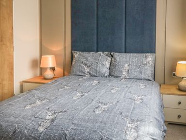 A bedroom with a bed with deer print bedding two bedside tables with lamps and a panelled headboard at Daisy Lodge in Cayton Bay near Cayton
