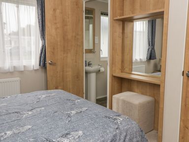 A bedroom with a bed a mirror a stool and a door leading to a bathroom at Daisy Lodge in Cayton Bay near Cayton