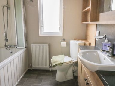 A bathroom with a bathtub shower toilet sink towel and wooden cabinets at Daisy Lodge in Cayton Bay near Cayton
