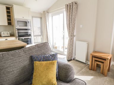 A living area with a gray sofa with cushions and wooden nesting tables near a radiator and sliding glass door at Daisy Lodge in Cayton Bay near Cayton