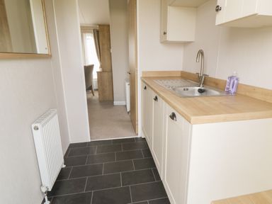 A narrow kitchen with a sink and countertop and a doorway showing a room with a chair at Daisy Lodge in Cayton Bay near Cayton