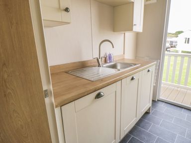 A kitchen countertop with a sink and faucet next to a sliding door with a view outside at Daisy Lodge in Cayton Bay near Cayton