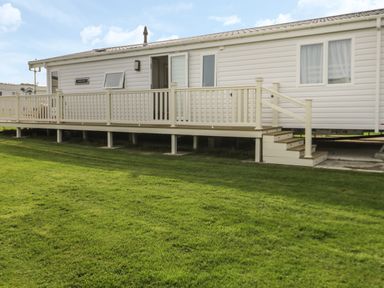 A white mobile home with a wooden deck and steps on a grassy lawn at Daisy Lodge in Cayton Bay near Cayton