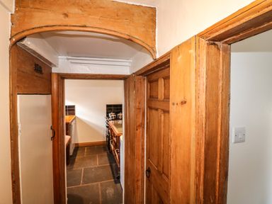A hallway with wooden door frames leading to a kitchen with a stove and countertop at Hops Cottage in Doveridge