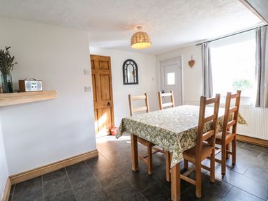 A dining room with a table covered by a patterned cloth and four wooden chairs at Hops Cottage in Doveridge