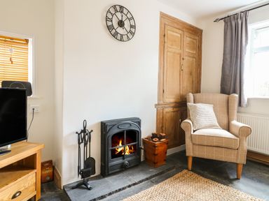 A living room with a fireplace an armchair a wooden cabinet and a television at Hops Cottage in Doveridge