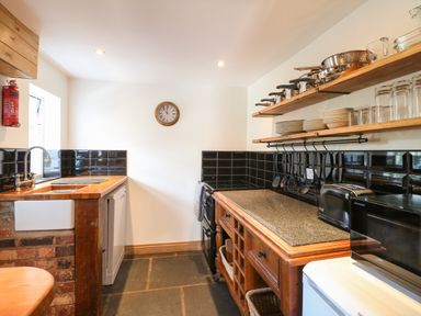 A kitchen with wooden counters black tile backsplash shelves with dishes and pots a microwave toaster and stove at Hops Cottage in Doveridge
