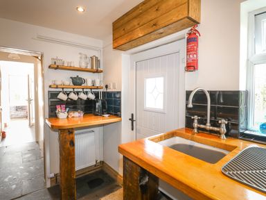 A kitchen with wooden countertops a sink a faucet shelves with cups and teapots and a white door at Hops Cottage in Doveridge