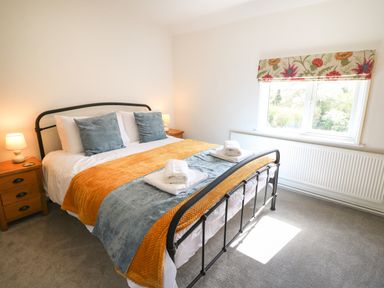 A bedroom with a bed covered with cushions and blankets next to a window at Hops Cottage in Doveridge
