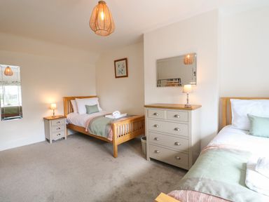 A bedroom with two single beds bedside tables lamps a dresser and a mirror at Hops Cottage in Doveridge
