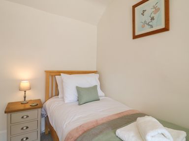A bedroom with a single bed beside a bedside table with a lamp and painting on the wall at Hops Cottage in Doveridge