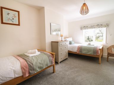 A bedroom with two single beds a chest of drawers a mirror a window and a wicker chair at Hops Cottage in Doveridge