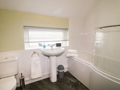 A bathroom with a toilet a pedestal sink a bathtub with towels and a window with blinds at Hops Cottage in Doveridge