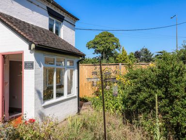 Exterior of a white cottage with a garden and bird feeders at Hops Cottage in Doveridge