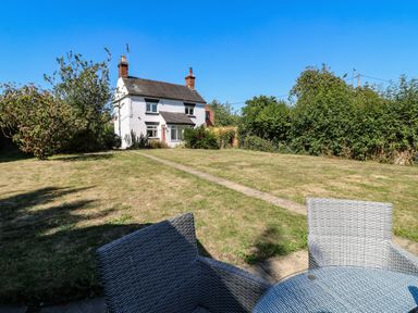 A backyard with lawn chairs and a table overlooking a white two-story house at Hops Cottage in Doveridge