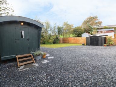 A gravel yard with a dark green shed a black metal storage shed potted plants and wooden fence at Hazel Nook in Narberth