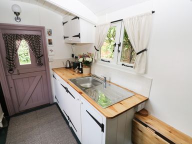 A kitchen with a wooden countertop a stainless steel sink and a purple door with curtains at Hazel Nook in Narberth