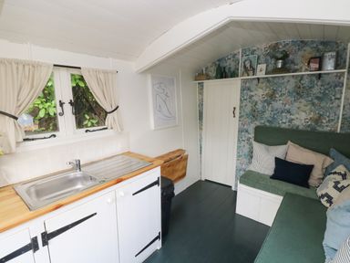 A small kitchen and seating area with a sink, green cushioned bench, and patterned wall at Hazel Nook in Narberth