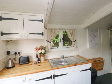 A kitchen with a wooden countertop, a sink, appliances, flowers on the counter, and a window with curtains at Hazel Nook in Narberth