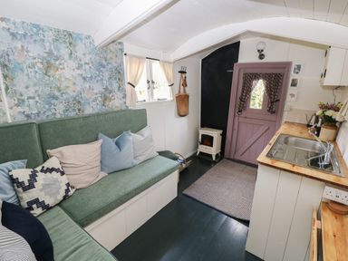 A small room with a green cushioned bench sofa and wooden countertop with a sink next to a purple door at Hazel Nook in Narberth