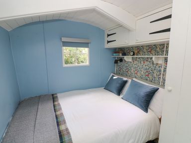A bedroom with a bed with blue pillows a window and shelves above the bed at Hazel Nook in Narberth
