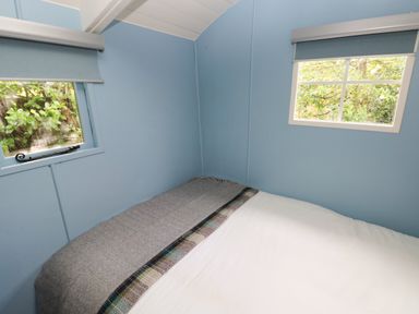 A small bedroom with blue walls two windows and a bed with a white duvet and grey blanket at Hazel Nook in Narberth