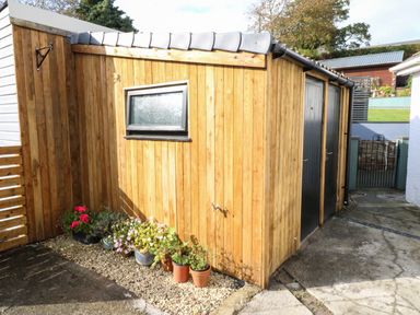 An outdoor wooden shed with black doors and a small window with flower pots on gravel at Hazel Nook in Narberth