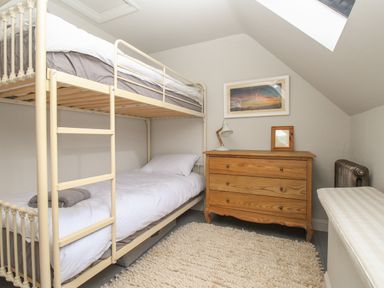 A bedroom with a bunk bed a wooden chest of drawers a lamp a painting and a rug at St Marys Chapel in West Lulworth