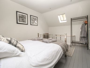 A bedroom with a bed, gray blanket, folded towels, clothes rack with robes, framed pictures on the wall, and a skylight window at St Mary's Chapel in West Lulworth