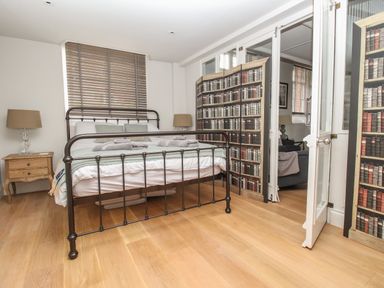 A bedroom with a metal bed frame nightstands with lamps wooden blinds and a folding screen with book designs at St Mary's Chapel in West Lulworth