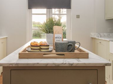 A kitchen island with a wooden tray holding two mugs muffins a coffee bag and a plant at St Mary's Chapel in West Lulworth