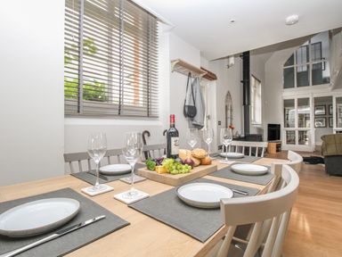 A dining table set with plates wine glasses and a cheese board in a room with a wood stove and large windows at St Marys Chapel in West Lulworth