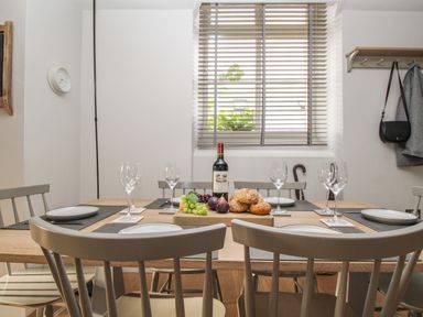 A dining table set with plates wine glasses bread fruit and a bottle of wine in a room with a window at St Mary's Chapel in West Lulworth