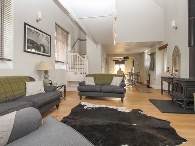 A living room with two grey sofas a cowhide rug a wood stove and a dining area in the background at St Marys Chapel in West Lulworth