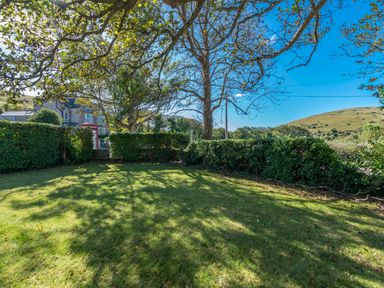 A grassy garden area with trees and hedges near a stone building and hills at St Marys Chapel in West Lulworth